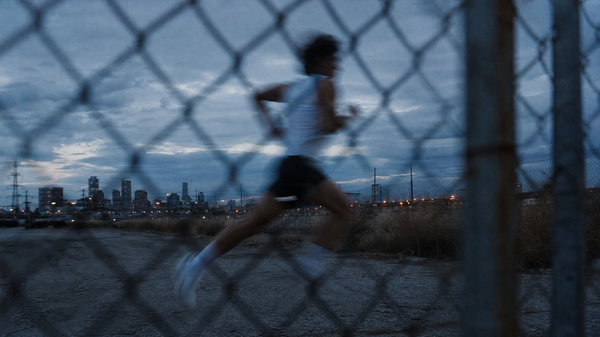 Generated_with_Kive.ai_-_Young_athletic_man_running_at_dusk_through_urban_outskirts__shot_through_a_chain-link_fence_creating_a_blurred_foreground_layer__extreme_motion_blur_on_the_su.png